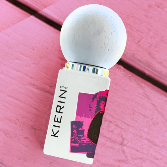 Perfume bottle with a spherical cap, labeled "KIERIN NYC," lies on a pink wooden surface.